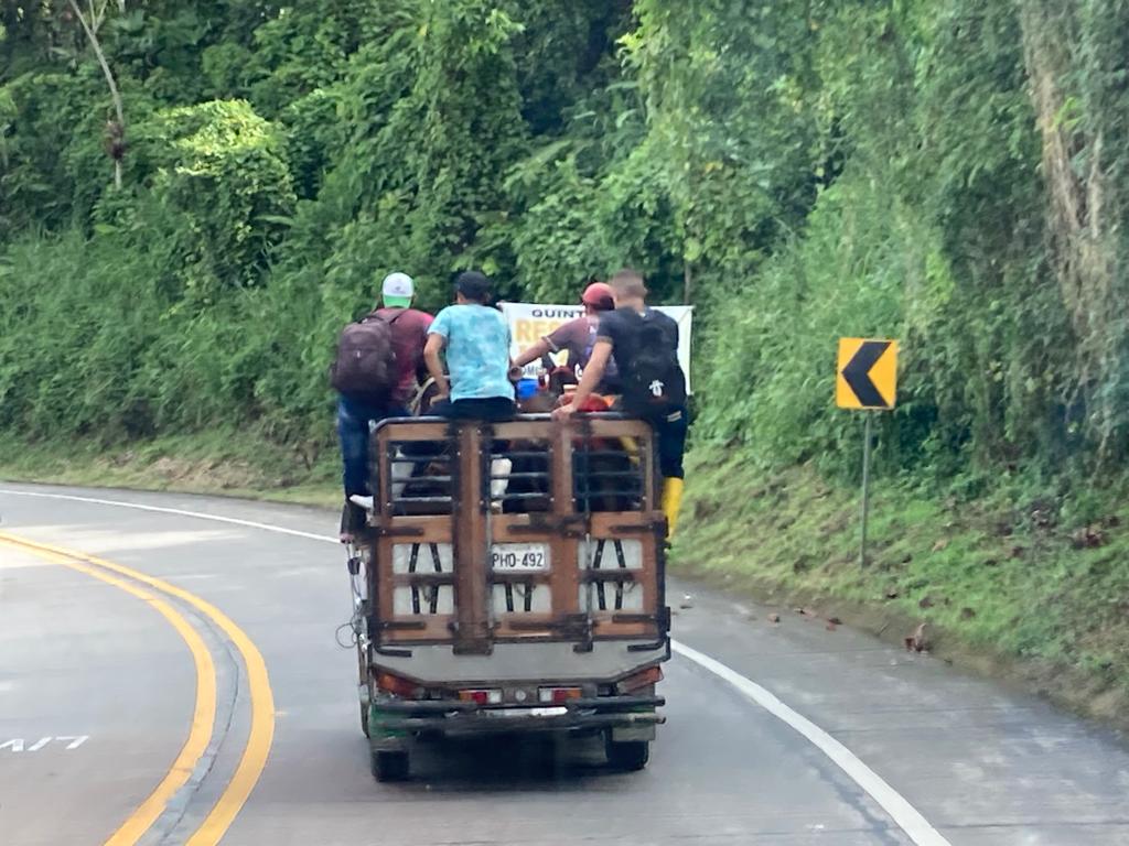 Several people riding on the open back of a truck along a highway.