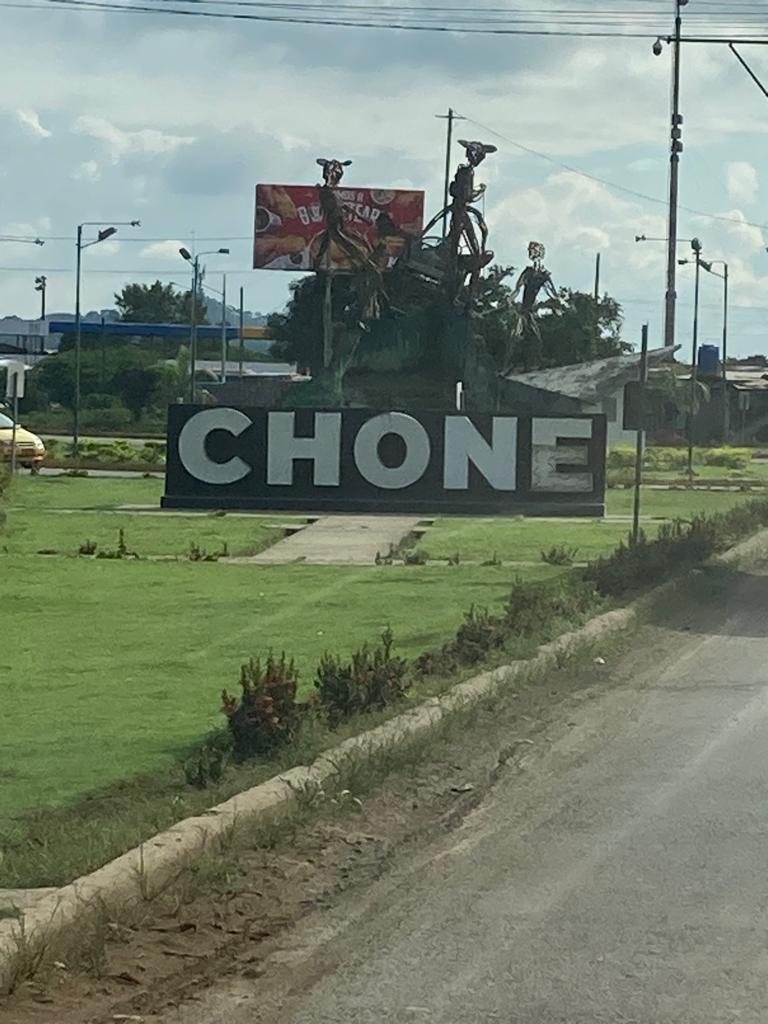 A "CHONE" town welcome sign set in a grassy median.