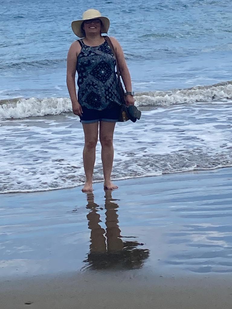 A woman in a sun hat and dress standing at the water's edge.