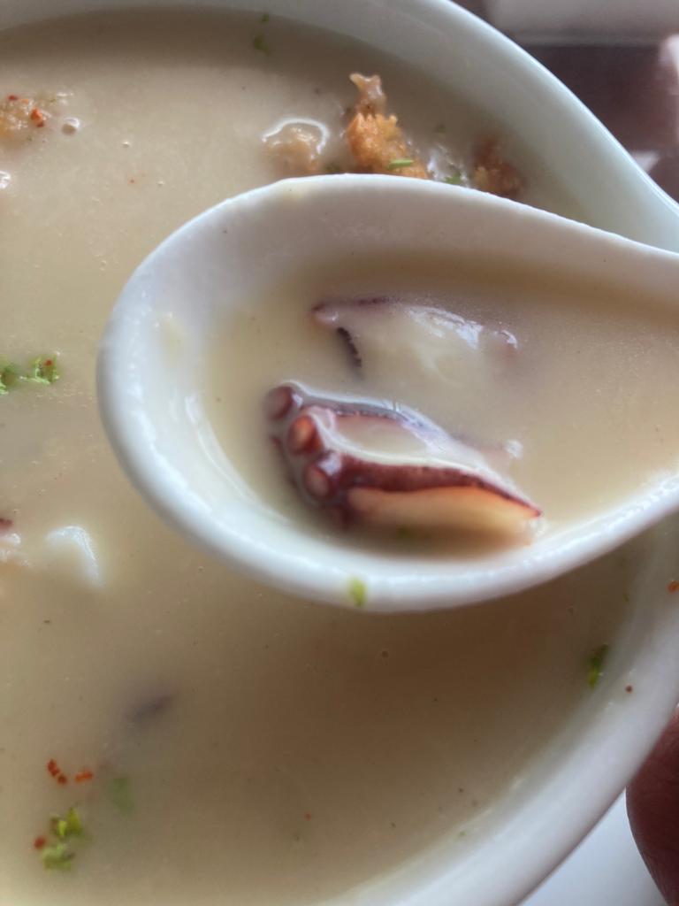 A close-up of a bowl of seafood soup with a spoon.