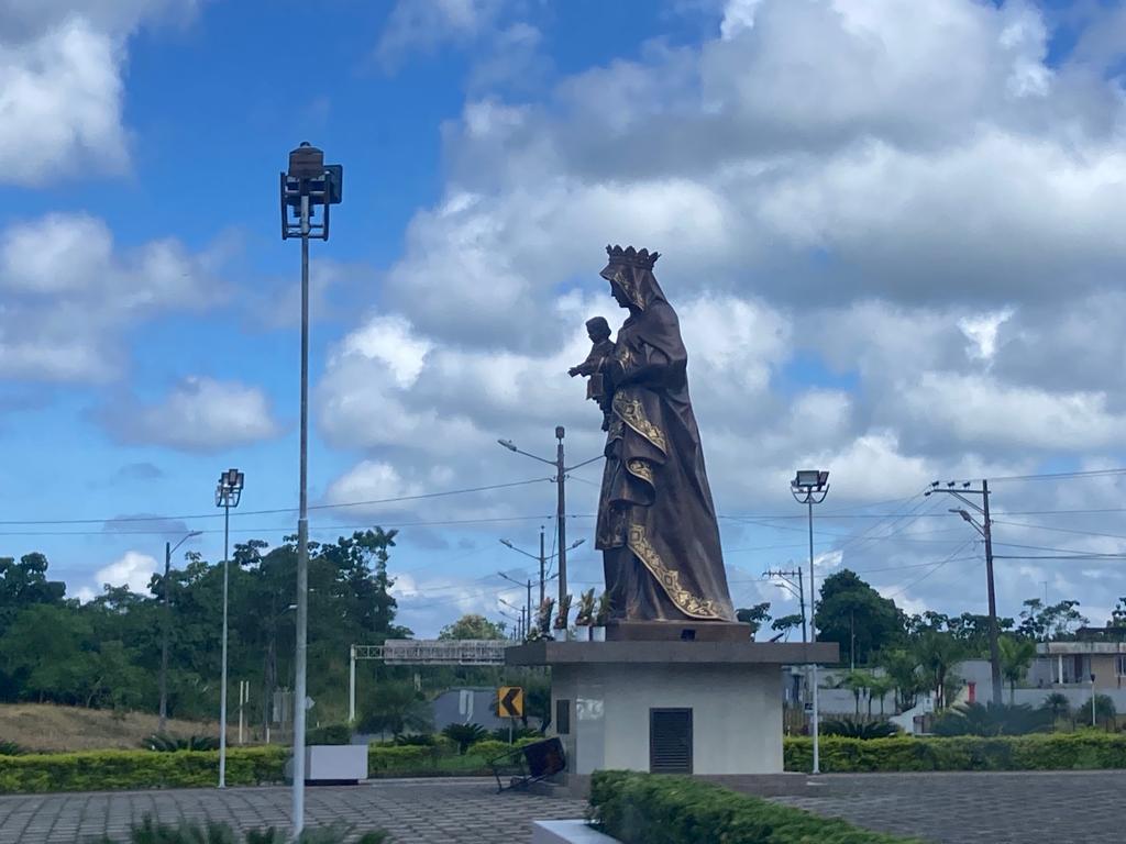 A tall statue of the Virgin Mary on a pedestal in a town plaza.