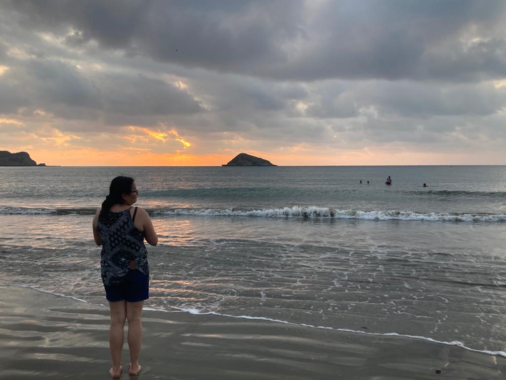 A woman photographing the sea as the sun sets behind an islet.