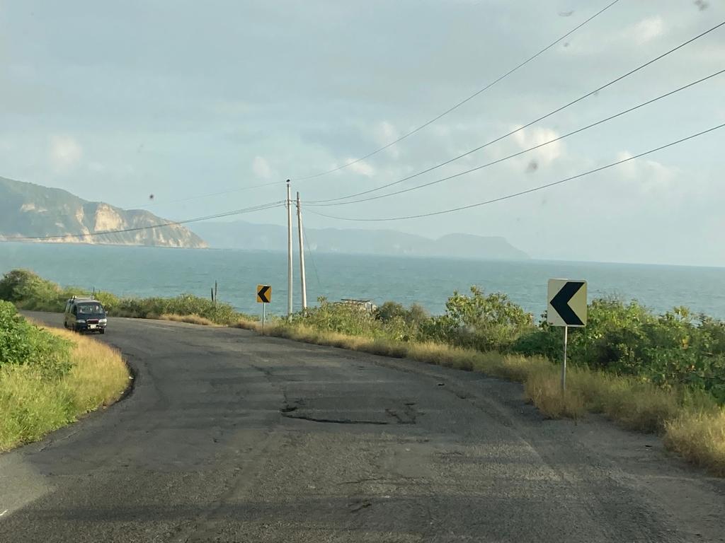 A coastal road curving toward the sea with headlands in the distance.