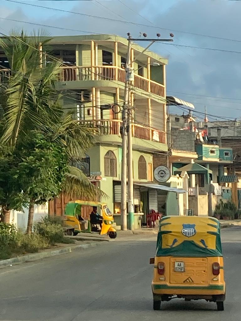 A yellow auto-rickshaw on a street in a coastal town.