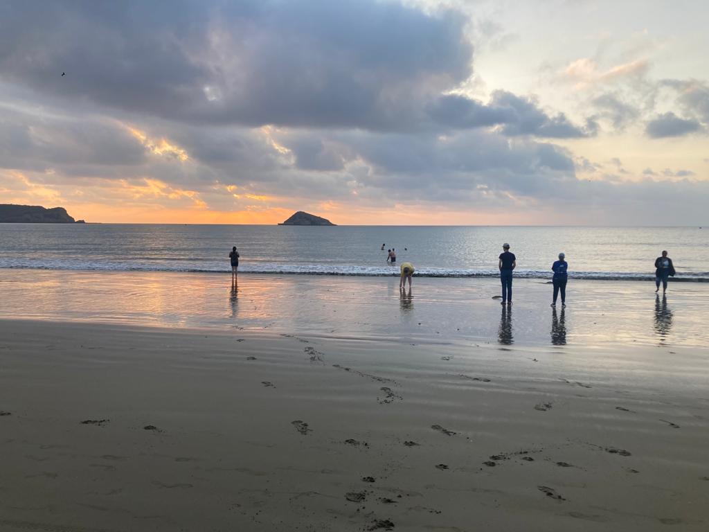 Silhouettes of people on the beach at sunset with reflections on the wet sand.