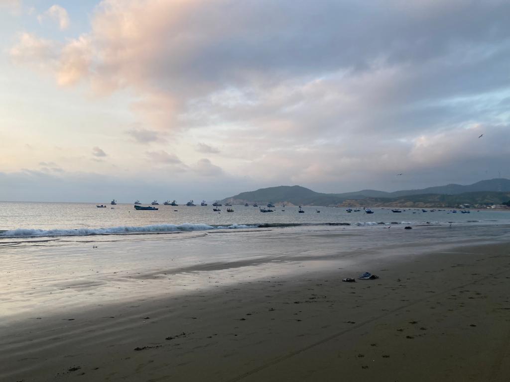 Fishing boats anchored offshore at a beach at sunset.
