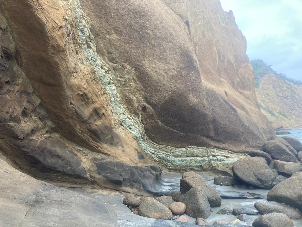 A layered rock cliff face meeting a boulder-strewn beach.