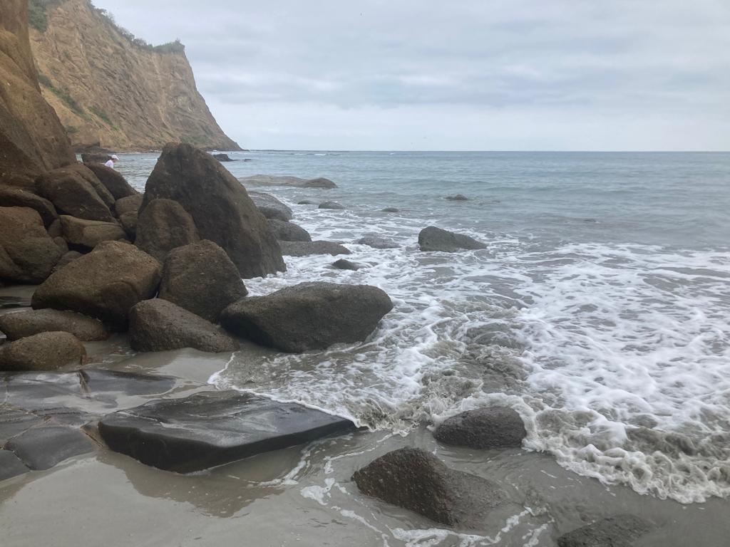 Waves crashing over boulders below a coastal cliff.