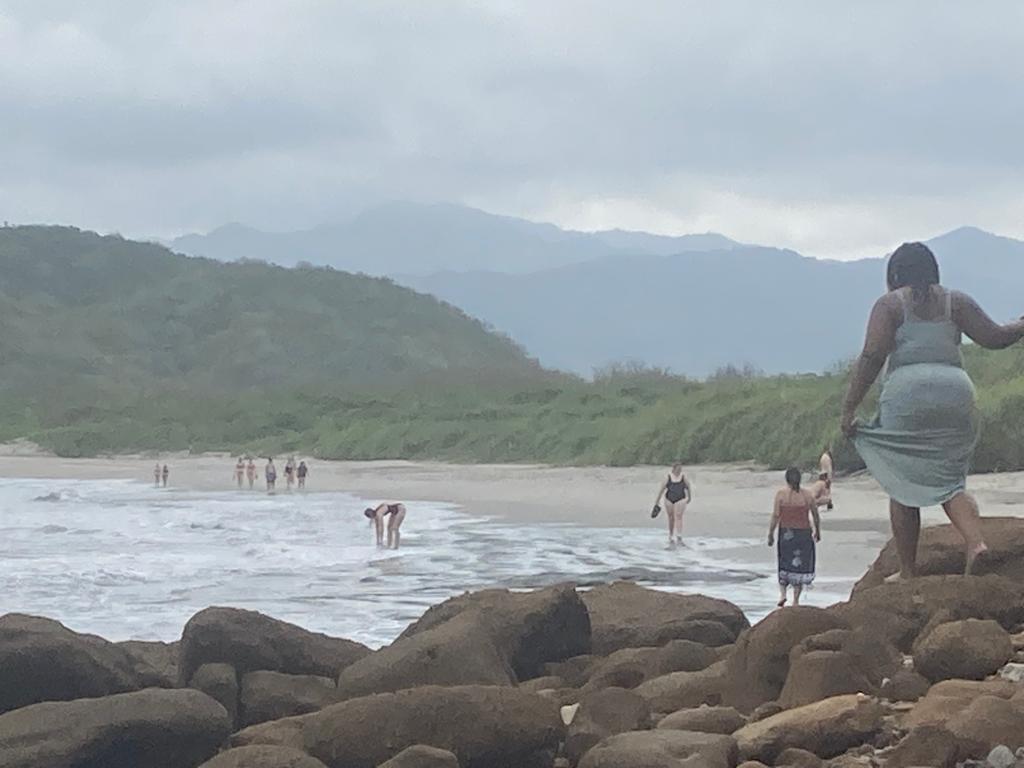 Beachgoers near large rocks with misty green hills behind.