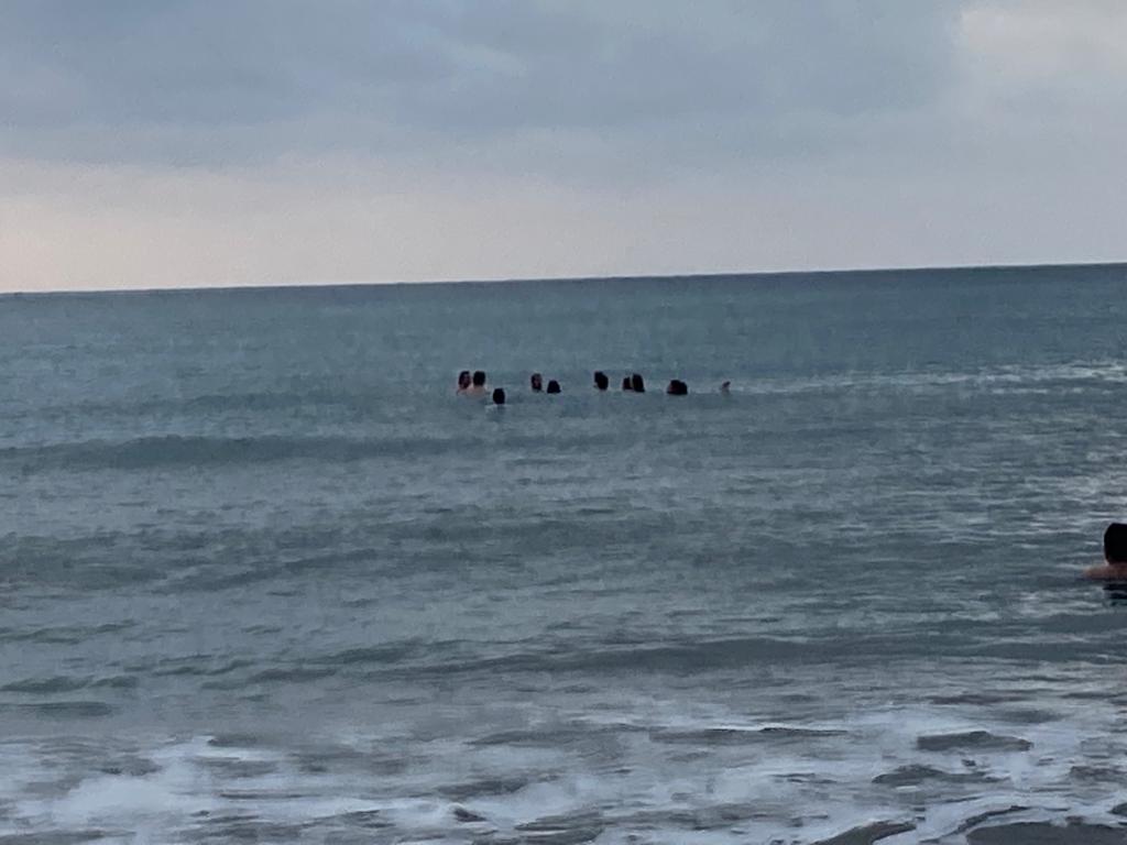 People wading in the ocean under a grey sky.