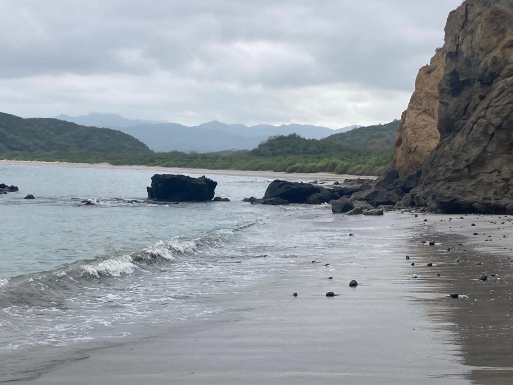 A rocky headland and cliffs at the end of a beach under grey skies.