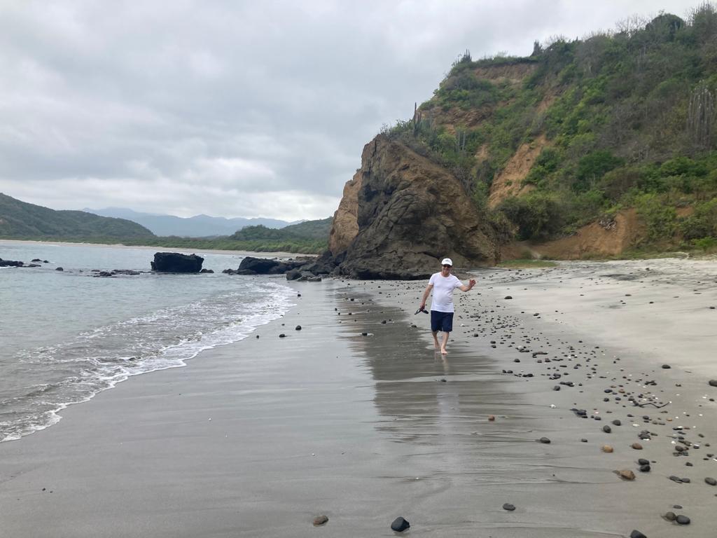 A person walking along a beach beneath tall coastal cliffs.