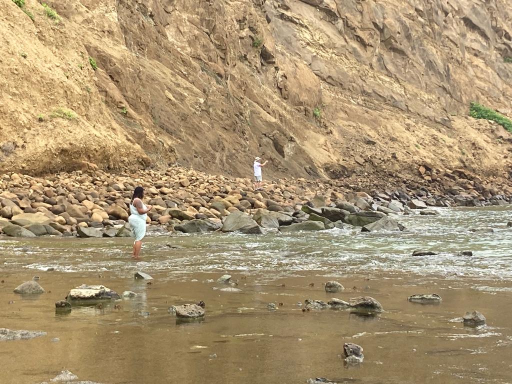 A person standing in a shallow stream beneath a tall cliff.