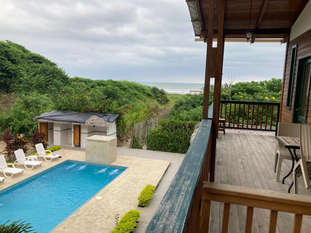 A view from a deck overlooking a poolside cabana and dunes.
