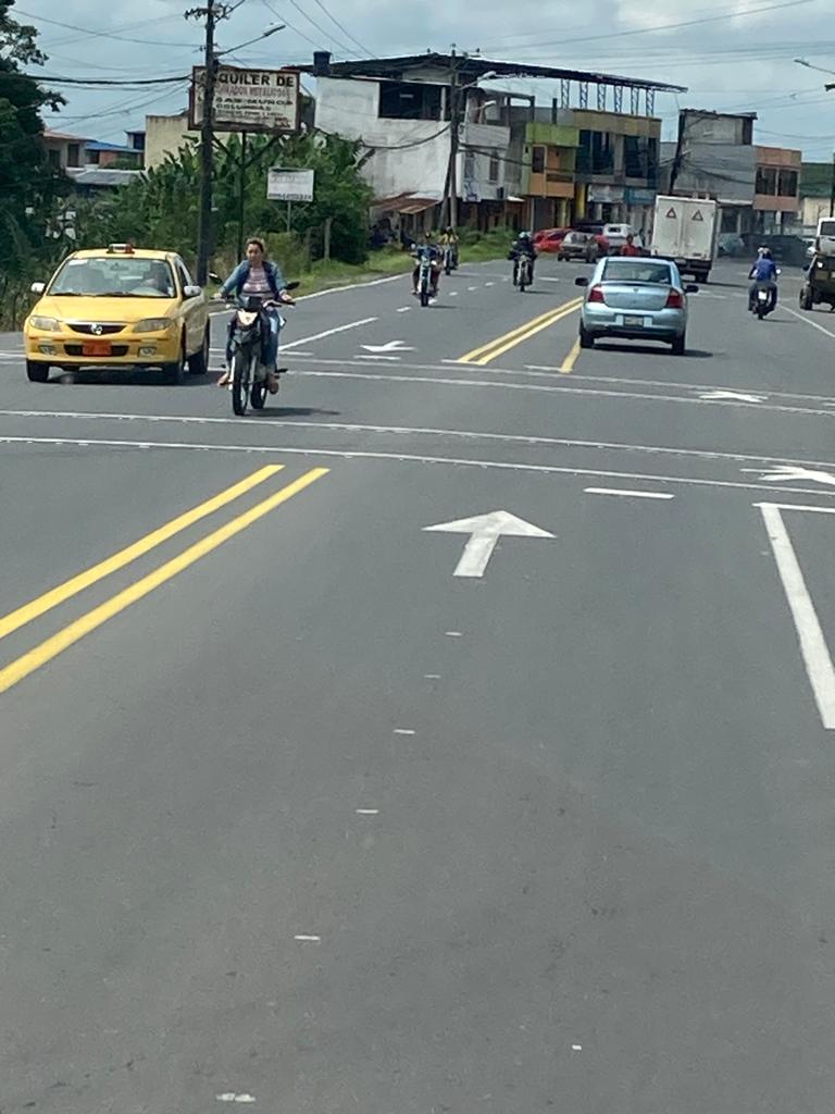 A yellow taxi and a motorcyclist traveling along a town street.