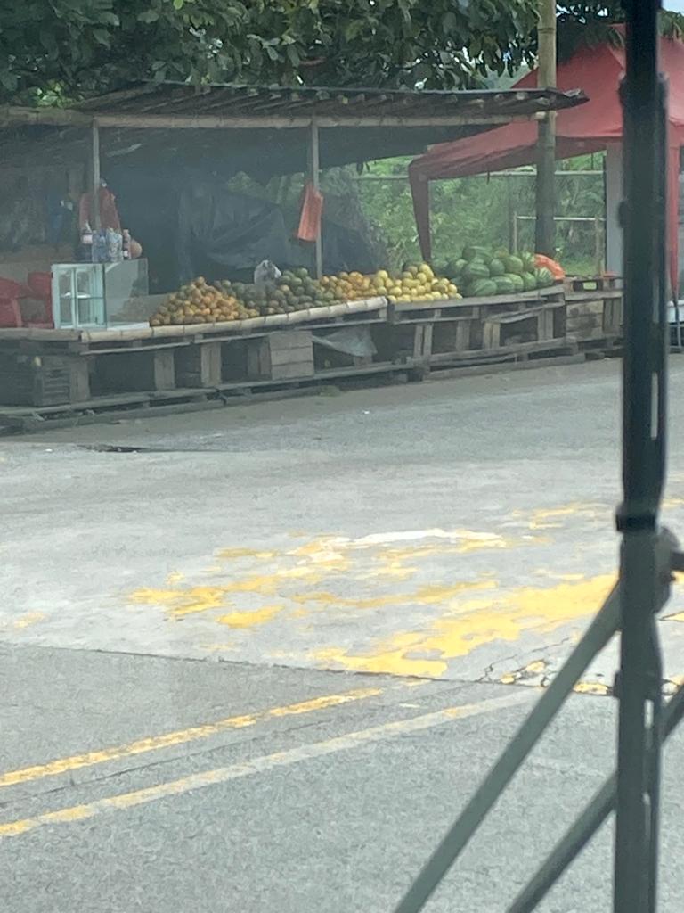 A roadside fruit and produce stand seen from a passing vehicle.