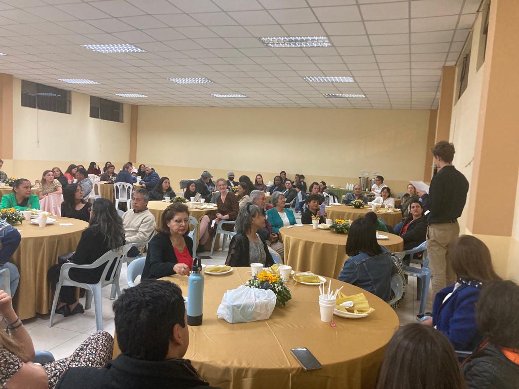 People seated at round tables during a community gathering.
