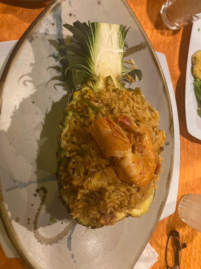 A plate of fried food served inside a hollowed pineapple.
