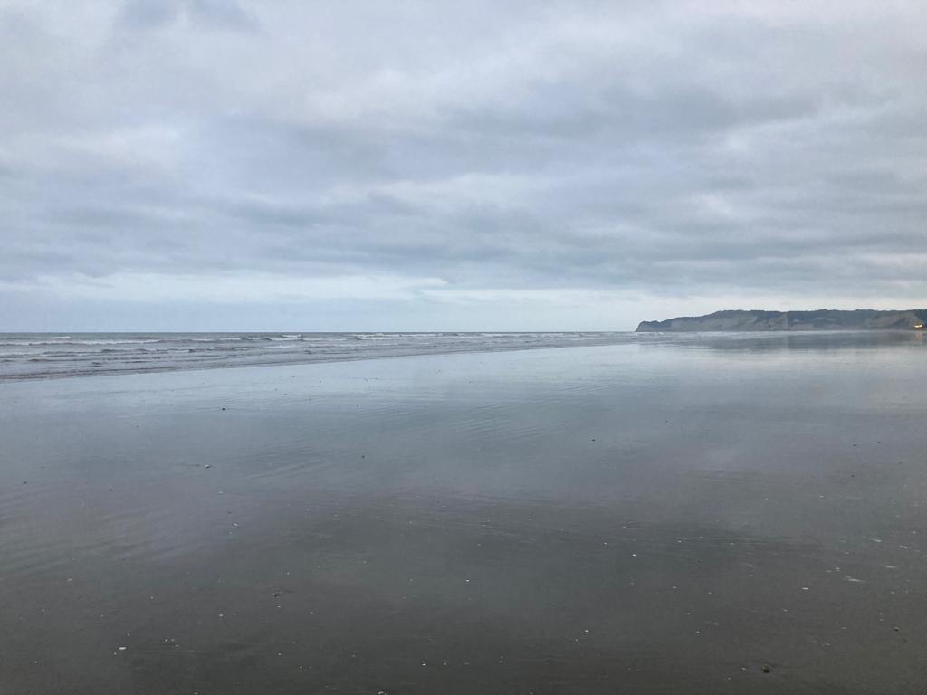 Still tidal flats meeting the sea beneath an overcast sky.
