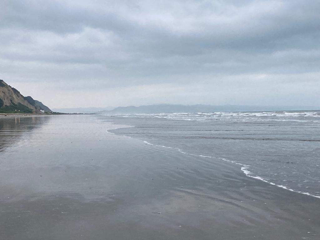 An expansive beach with a headland in the misty distance.
