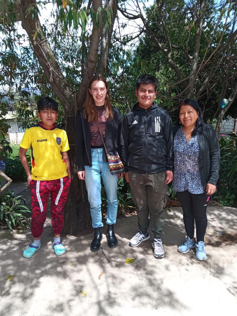 A student standing with a host family among trees.
