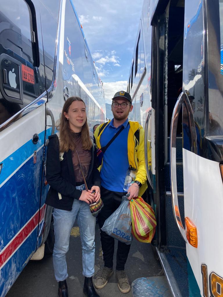A woman and companions posing beside a bus before departure.
