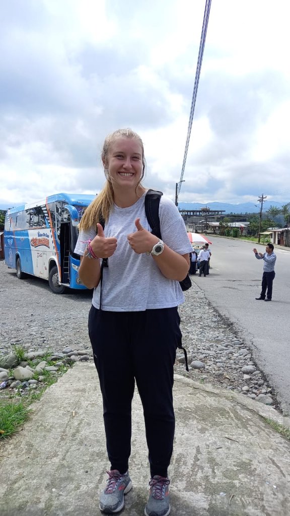 A student giving a thumbs-up beside a bus on a street.
