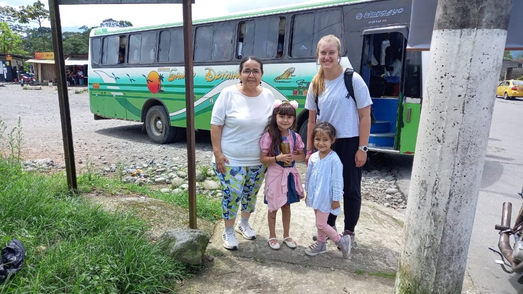 A student posing with a host family in front of a green bus.
