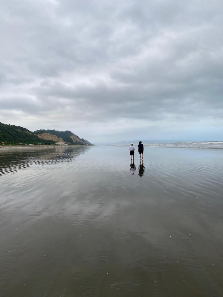 Two people standing far out on a mirror-calm tidal flat.
