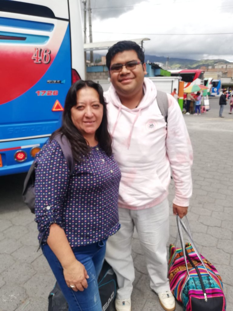 A woman and a man posing beside a bus at a terminal.
