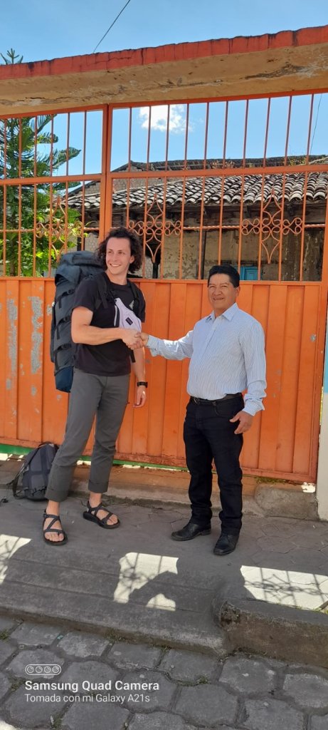 A student greeting a host family member at a doorway gate.
