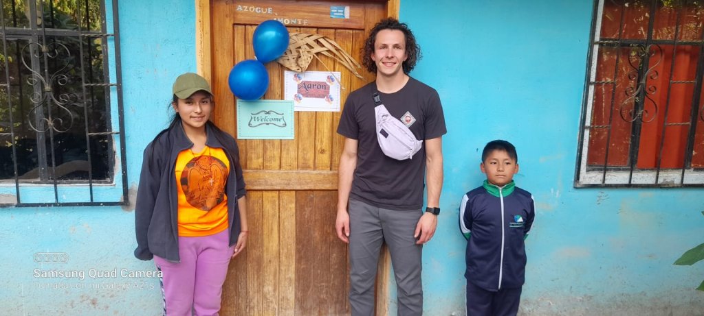 A student posing with host children at a home's front door.

