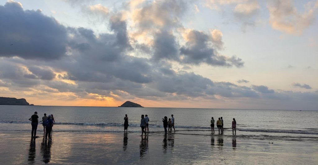 A group of people watching the sunset on a beach beside an islet.