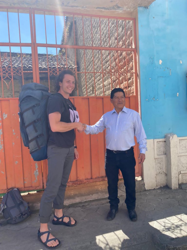A student with a backpack shaking hands with a host family member outside.
