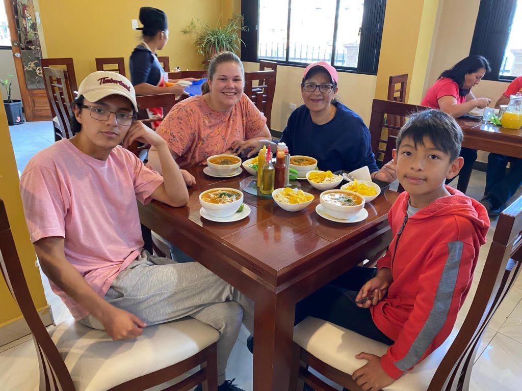 A student sharing a meal with a host family at a dining table.
