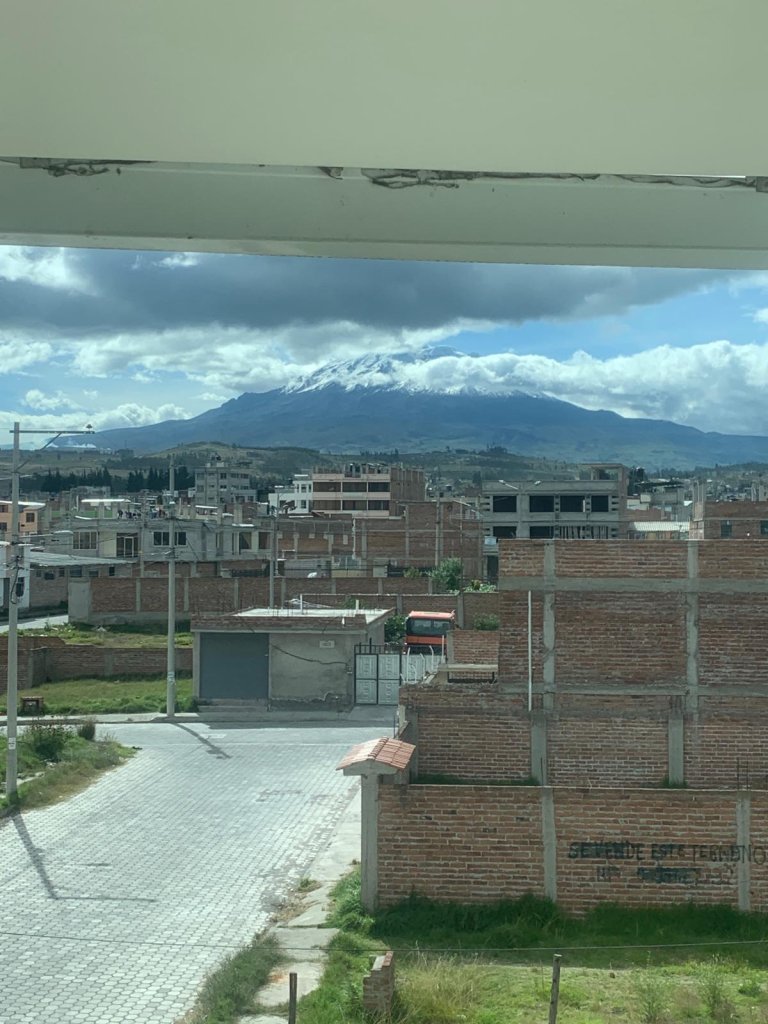 A view of hillside houses and mountains through a window.
