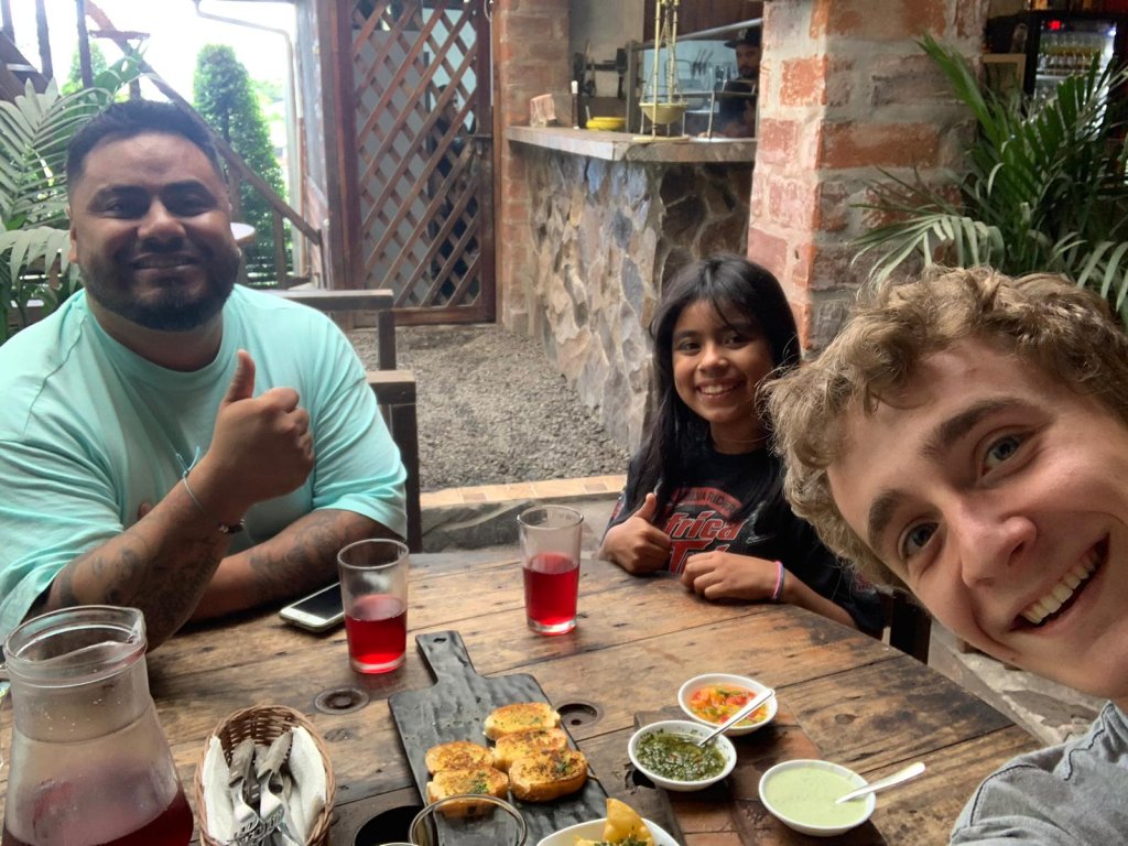 A student sharing a meal with a host family at an outdoor table.
