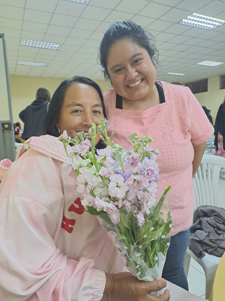 Two women smiling as one holds a bouquet of flowers.
