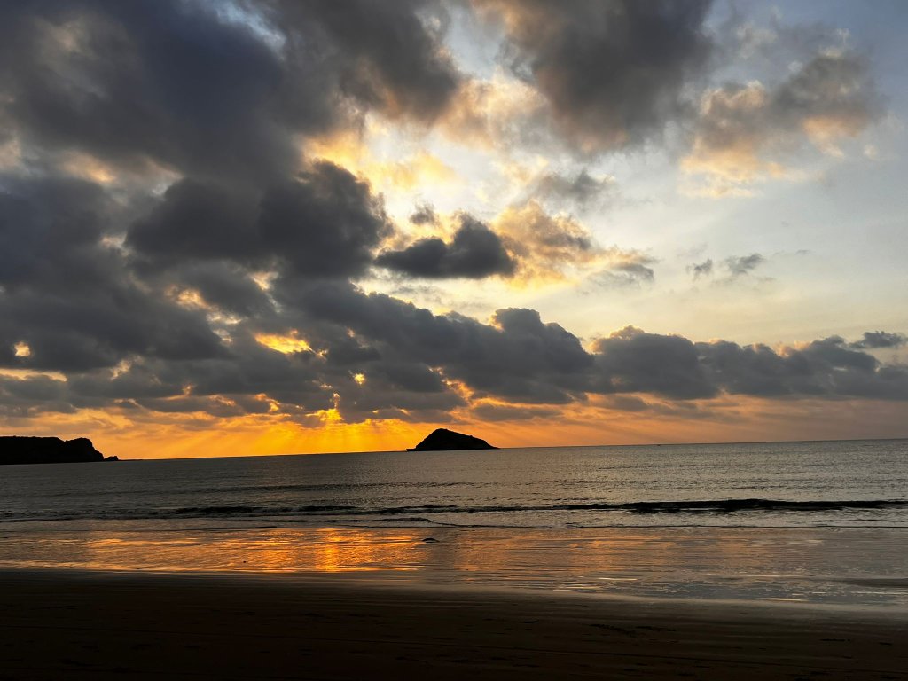 A dramatic cloudy sunset reflected on the wet beach.