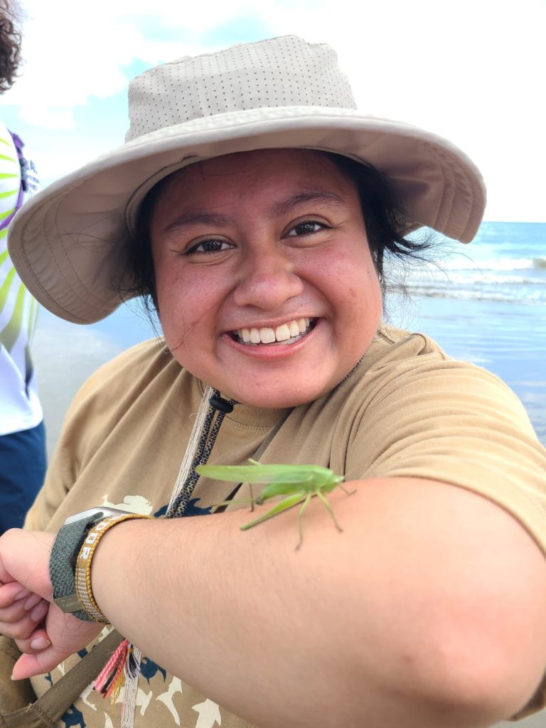 A smiling woman in a sun hat taking a selfie by the sea.