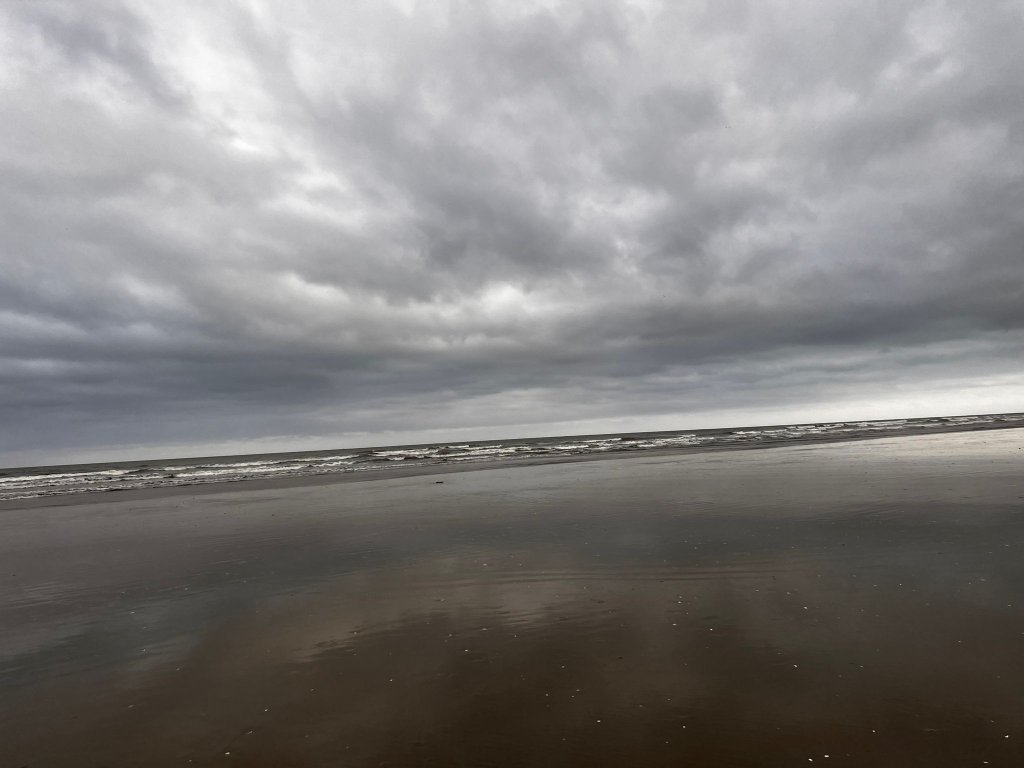 An overcast sky reflected on a wet, empty beach.
