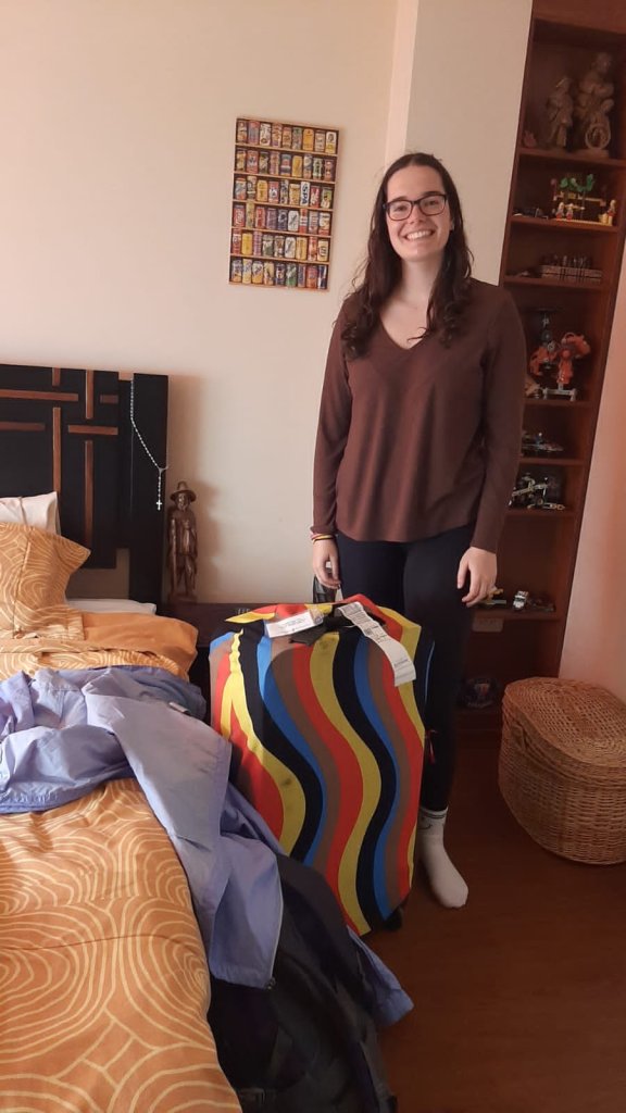 A student standing in a bedroom with a colorful woven blanket.
