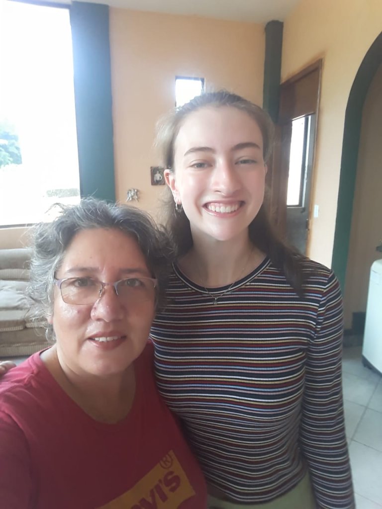 A student standing beside a smiling host family member indoors.
