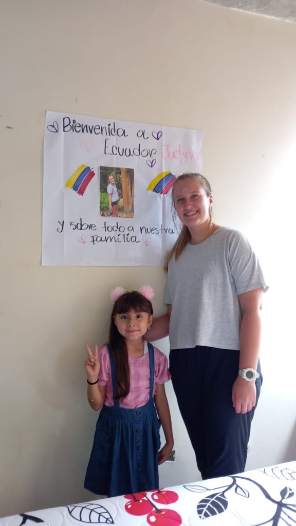 A student and a host child posing beside a welcome sign.
