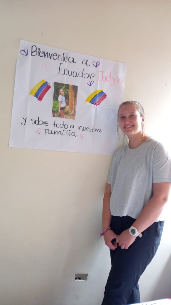 A student standing beside a handmade welcome poster.
