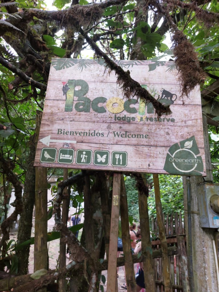 A wooden welcome sign for an eco-lodge among the trees.