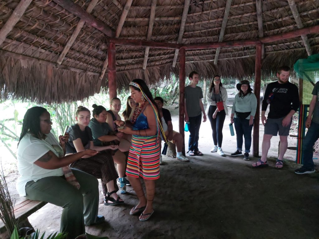A group gathered around a guide inside a thatched-roof hut.
