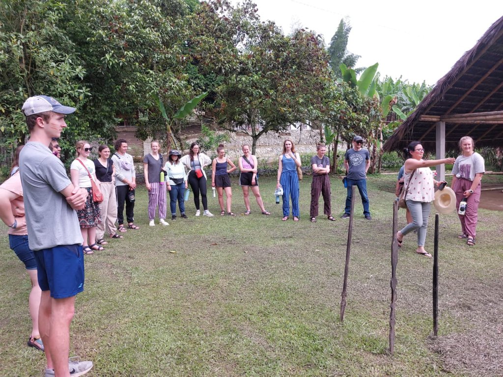 A group of students standing in a circle on a grassy lawn.
