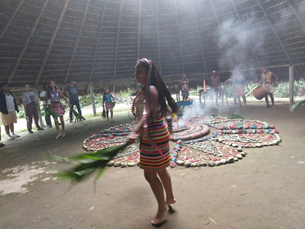 A woman in traditional dress performing beside a smoking central altar.

