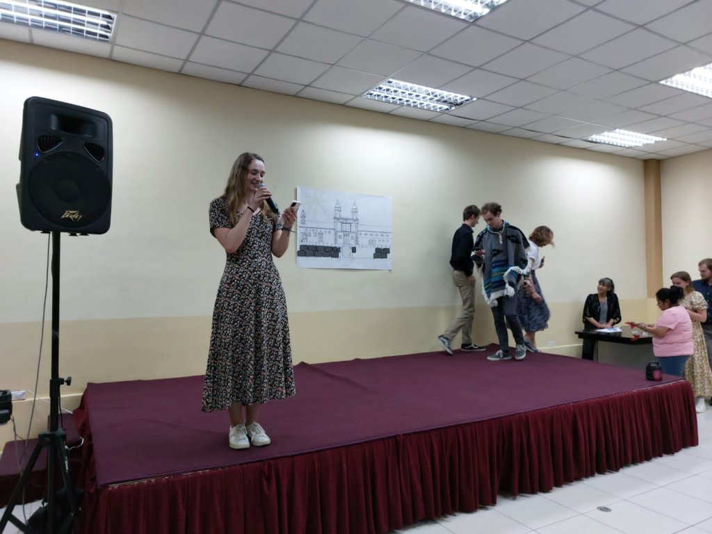 A woman speaking on a small stage before an audience.

